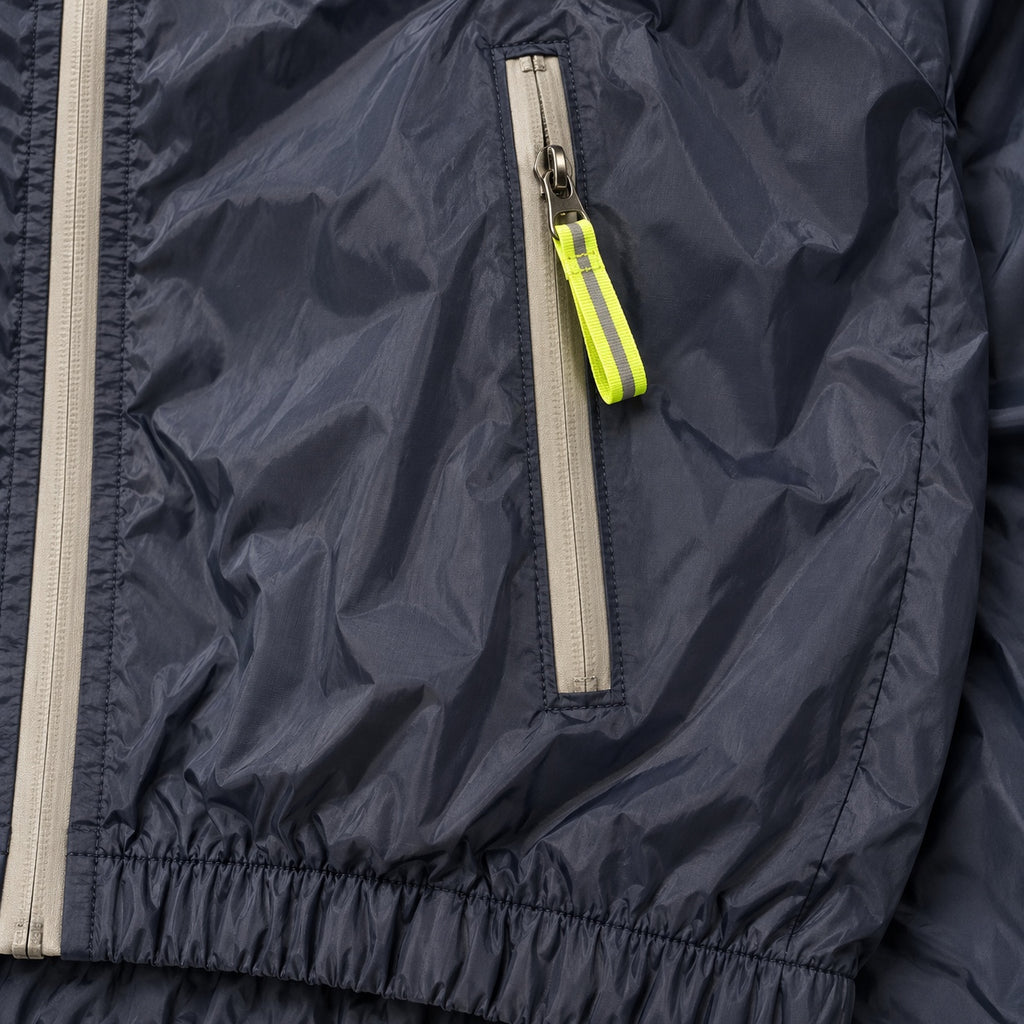 Close-up of a navy windbreaker pocket zipper, neon yellow-green pull and gathered hem.