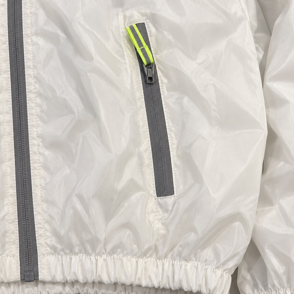Close-up of a white windbreaker pocket zipper, neon yellow-green pull and gathered hem.
